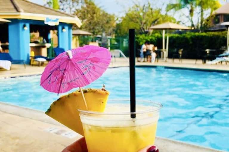 Yellow cocktail with pink umbrella by resort pool during daytime