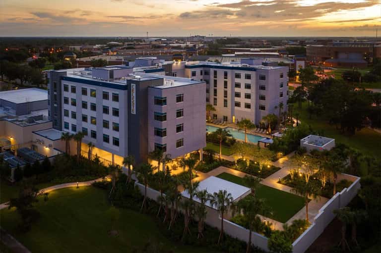 Contemporary multi-story hotel at dusk with illuminated grounds and pool area