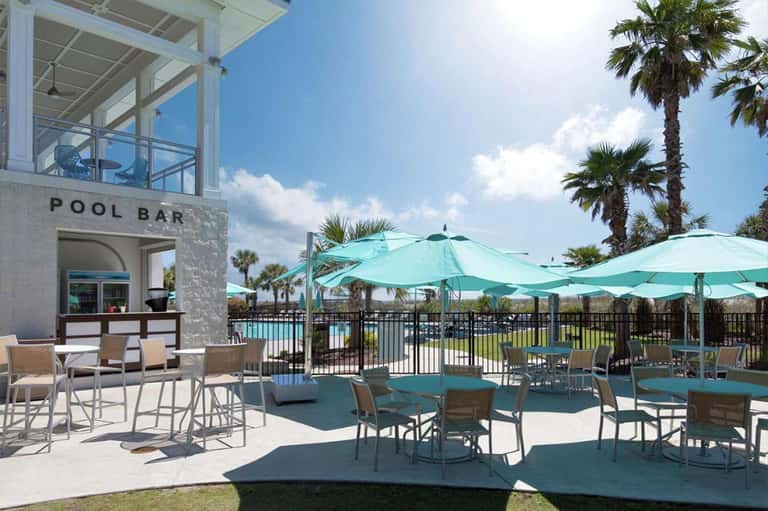 Pool bar area with turquoise umbrellas, lounge chairs, and palm trees under bright sunshine