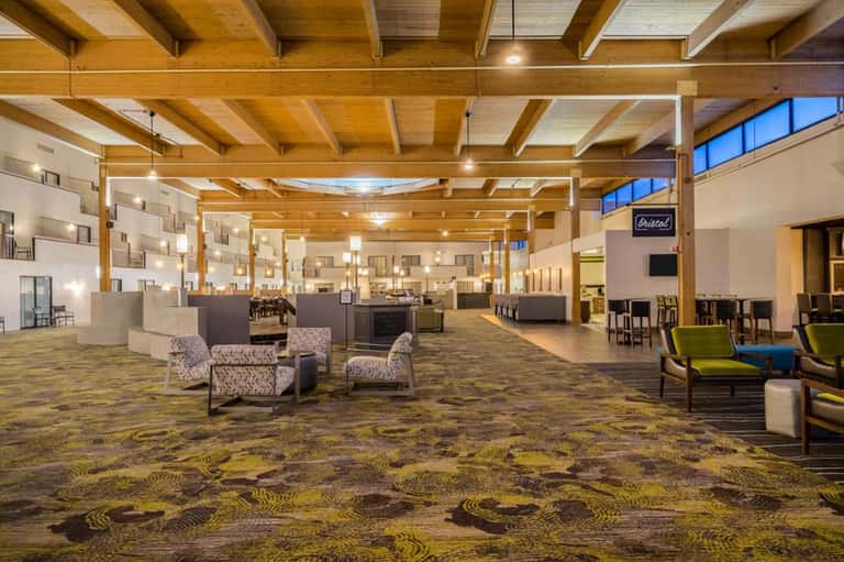 Modern hotel lobby with wooden beam ceiling, seating areas, and patterned carpet flooring