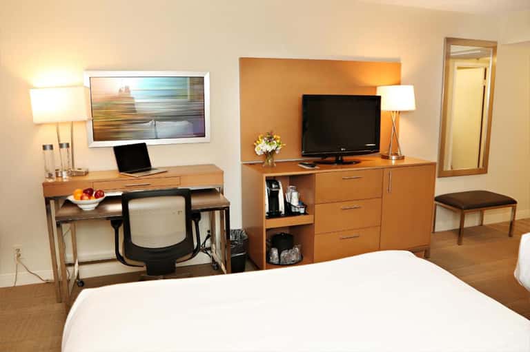 Hotel room with wood furniture, desk with laptop, TV, and neutral earth-tone decor