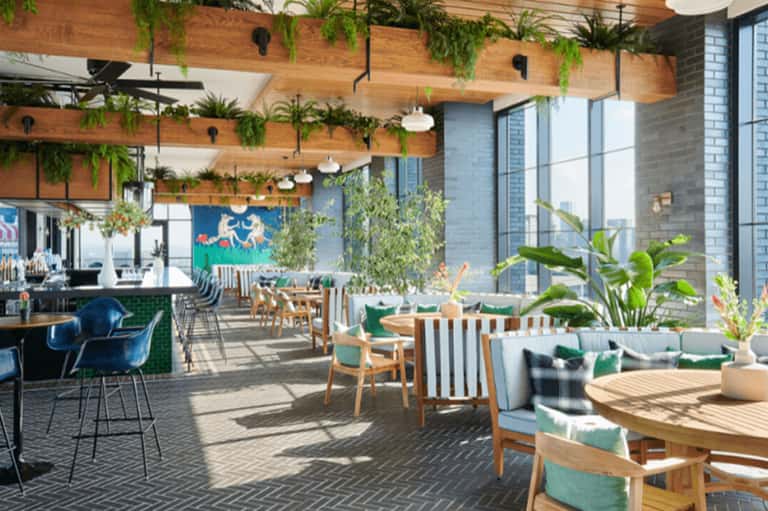 Modern rooftop lounge with wooden beams, hanging plants, natural wood furniture, and city views