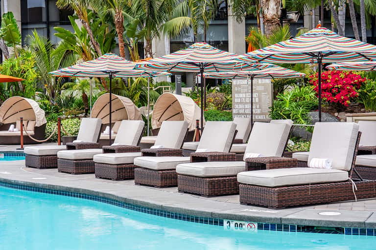 Poolside lounge area with striped umbrellas, wicker recliners, and tropical landscaping