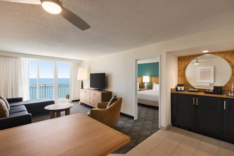 Hotel suite with ocean view balcony, living area, bedroom, and contemporary furnishings