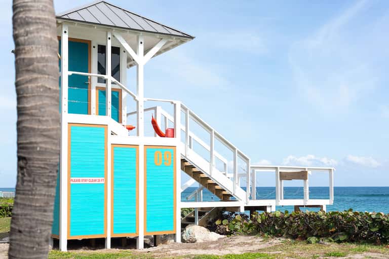 Colorful lifeguard tower with turquoise and orange trim on sandy beach near palm tree