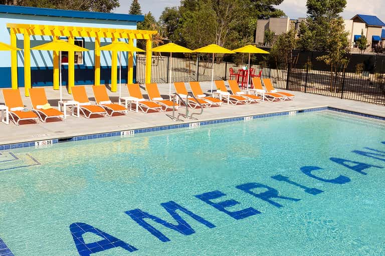Resort pool with turquoise water, orange loungers, yellow umbrellas, and cabana structures under clear sky