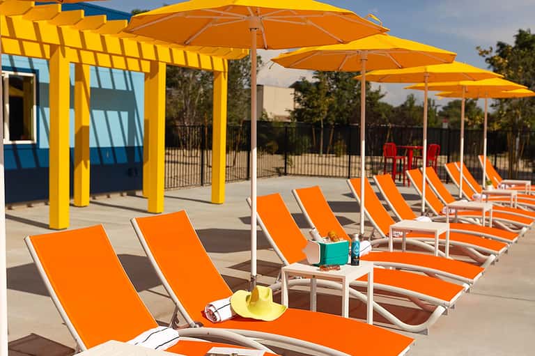 Rows of orange lounge chairs under yellow umbrellas and pergolas on a sunny patio