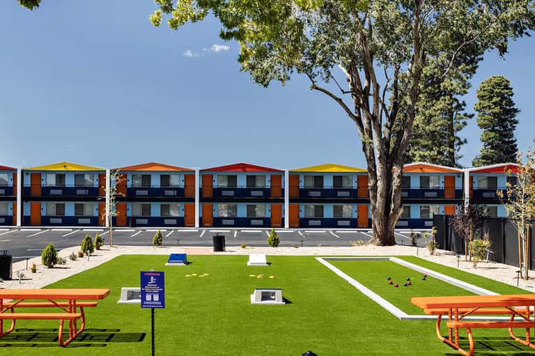 Modern orange and blue residential buildings with pitched roofs overlook a manicured lawn with picnic tables and large trees