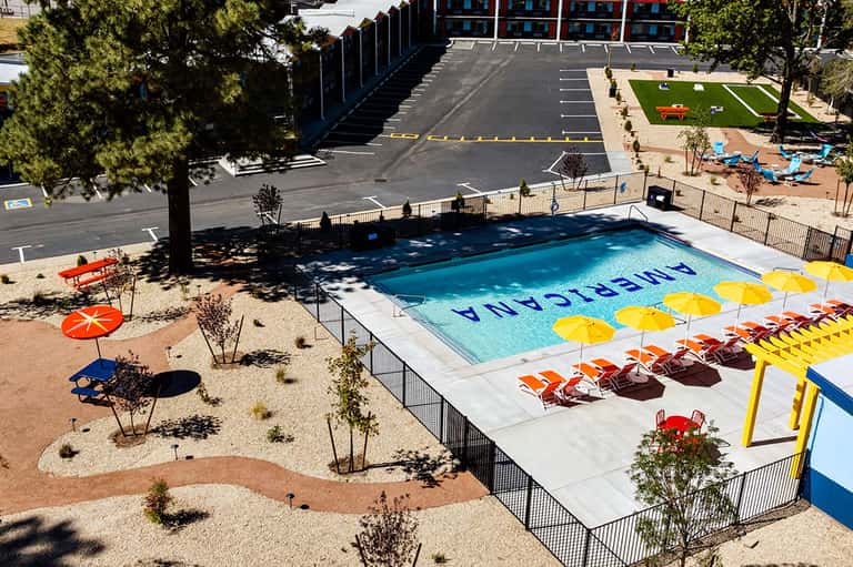 Modern pool deck with colorful umbrellas, loungers, sand area, and multi-story residential building