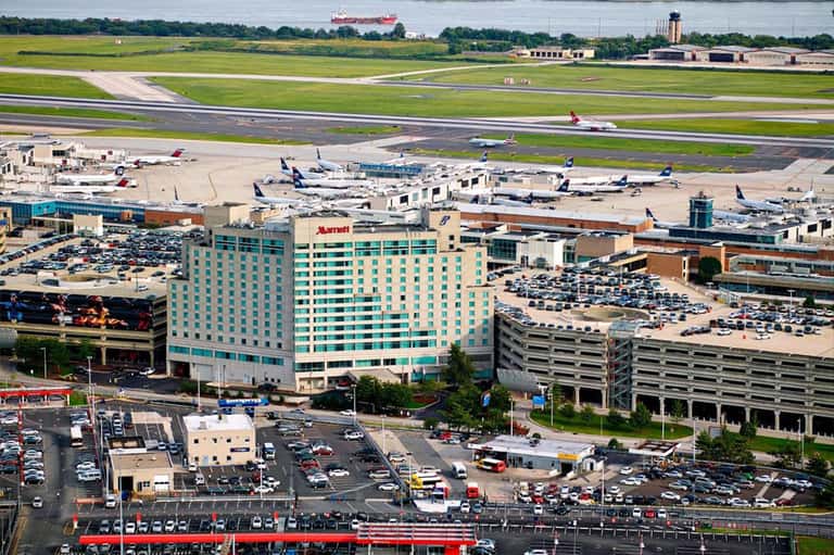 Airport hotel exterior with teal and cream facade, parking structures, and aircraft in background