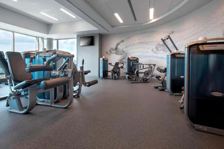 Modern gym with exercise equipment, blue accent walls, and large windows with city views