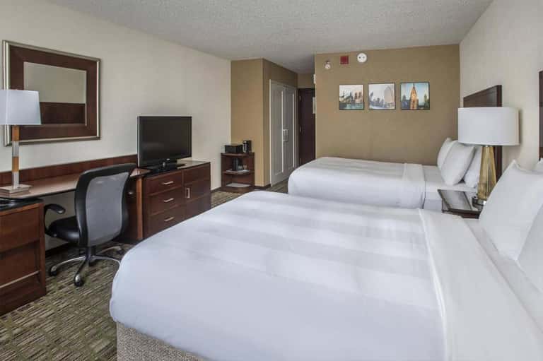 Modern hotel room with two queen beds, work desk, TV, and contemporary furnishings