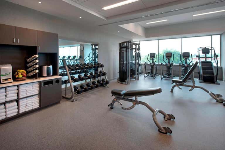 Modern fitness center with cardio equipment, weight racks, dumbbells, and large windows overlooking landscape