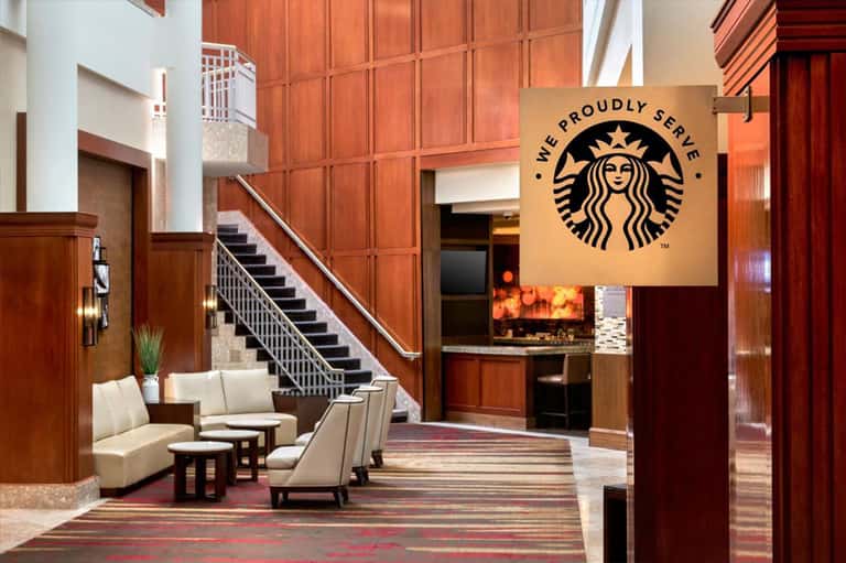 Upscale hotel lobby with wooden paneling, grand staircase, and Starbucks café