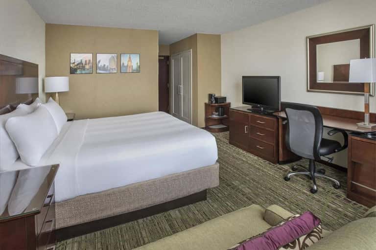 Hotel room with queen bed, desk, TV, and modern furnishings with beige and brown tones