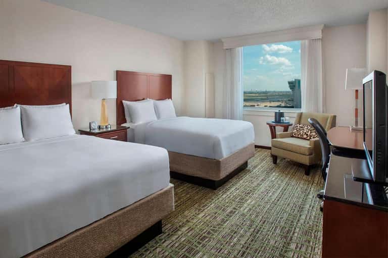 Hotel room with two queen beds, burgundy headboards, and panoramic window overlooking landscape