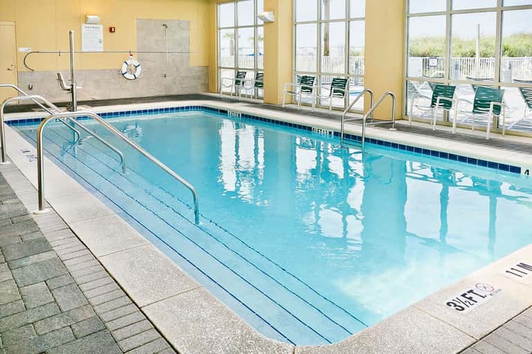 Indoor swimming pool with blue water, metal railings, and lounge chairs by the windows