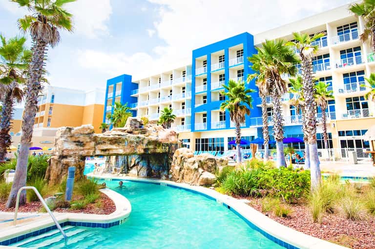 Bright blue and yellow resort buildings with turquoise lazy river and palm trees