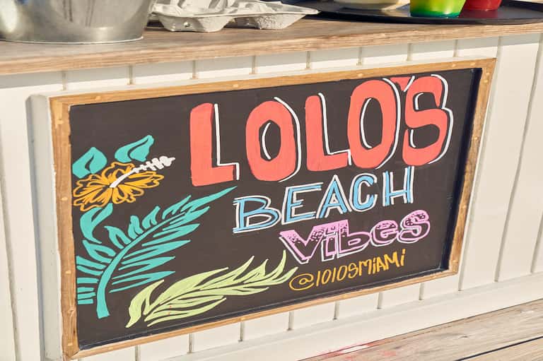 Chalkboard sign reading 'Lolos Beach Vibes' with colorful tropical leaf designs