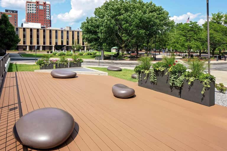 Urban rooftop terrace with metallic seating pods, planter boxes, and city park views