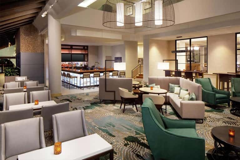 Hotel lobby lounge with green and beige seating, decorative lighting, bar area, and patterned carpeting