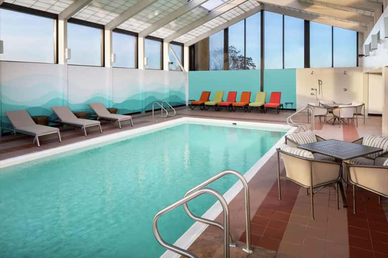 Indoor heated pool with turquoise water, lounge chairs, and mountain views through skylights
