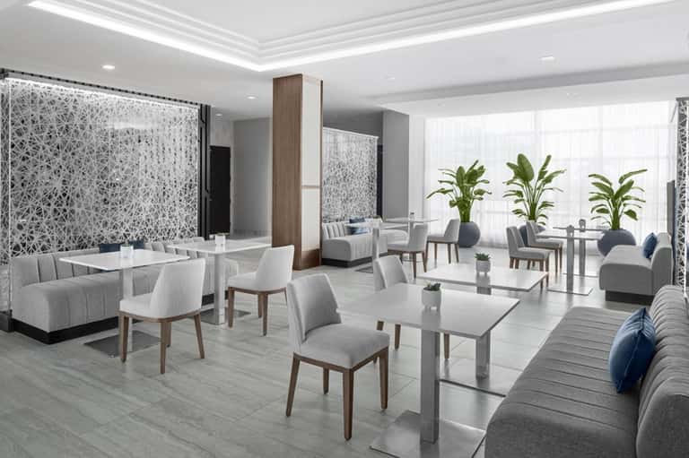 Modern hotel lounge with gray seating, decorative screens, potted plants, and natural light