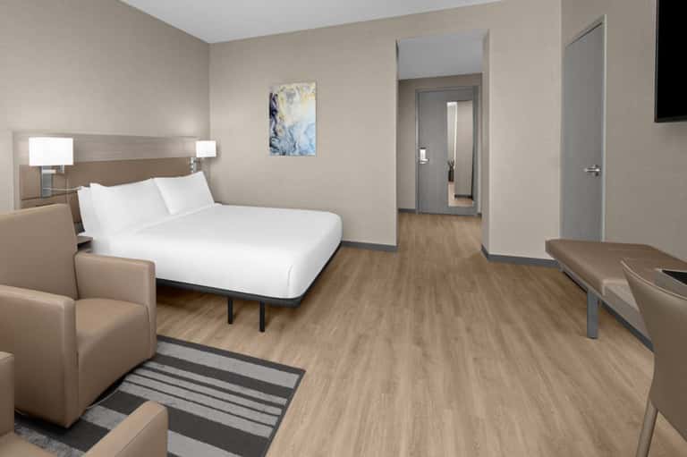 Contemporary hotel bedroom with queen bed, wood flooring, neutral tones, and ensuite bathroom