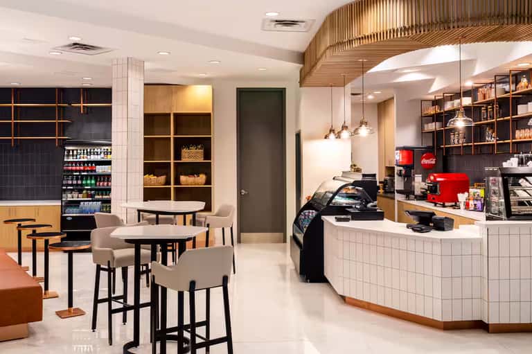 Modern café interior with wooden accents, white tile counter, pendant lights, and seating area