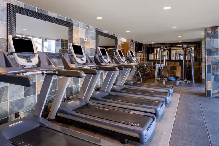 Modern fitness center with cardboard treadmills, mirrored walls, and stone tile flooring