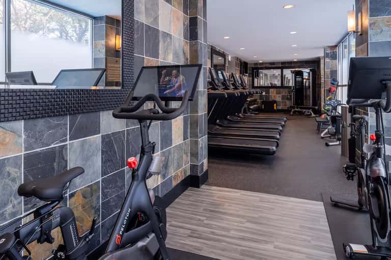 Modern fitness center with stationary bikes, treadmills, and exercise equipment along stone-tiled walls