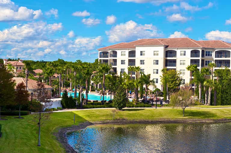 Resort exterior with white multi-story building, palm trees, and blue pool overlooking a lake