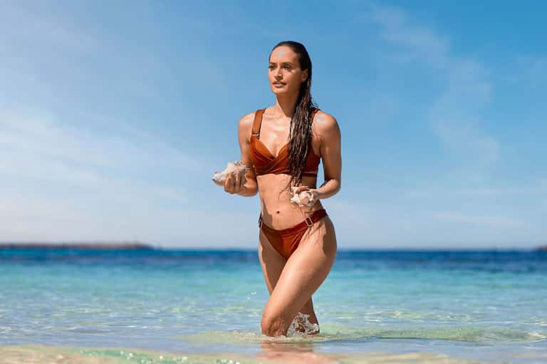 Woman in rust-colored bikini running into clear blue ocean water on a sunny beach day