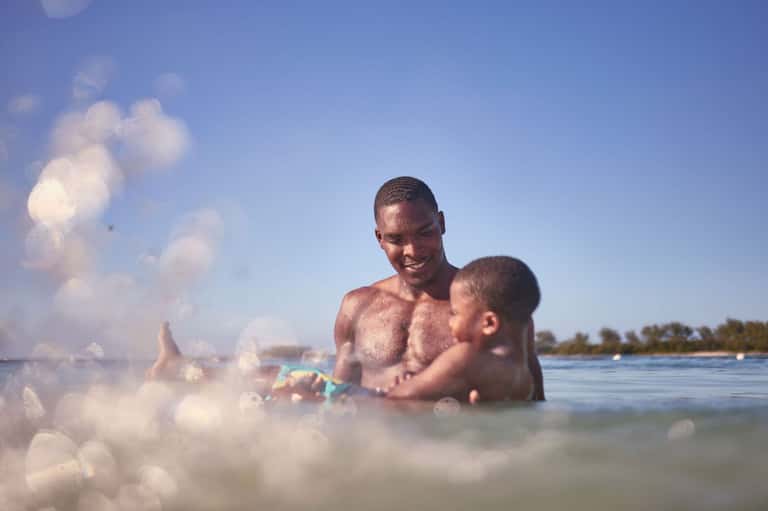 Father and son playing in shallow ocean waters on a sunny beach day