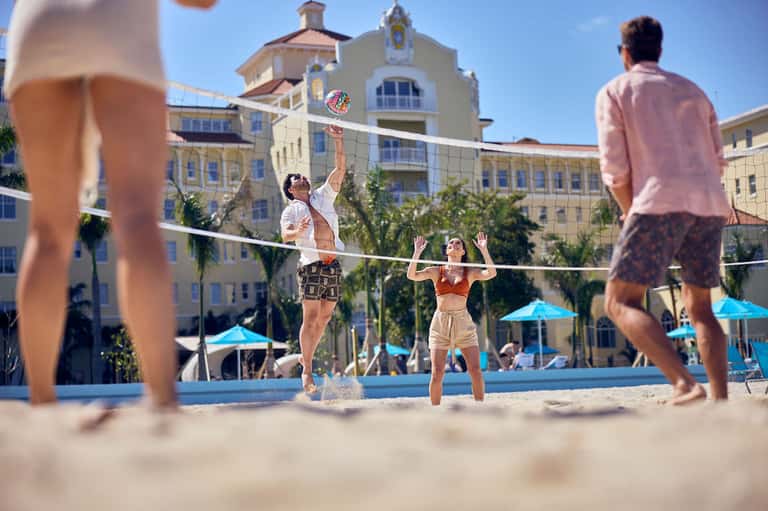 Beach volleyball game in front of yellow colonial-style hotel building with palm trees