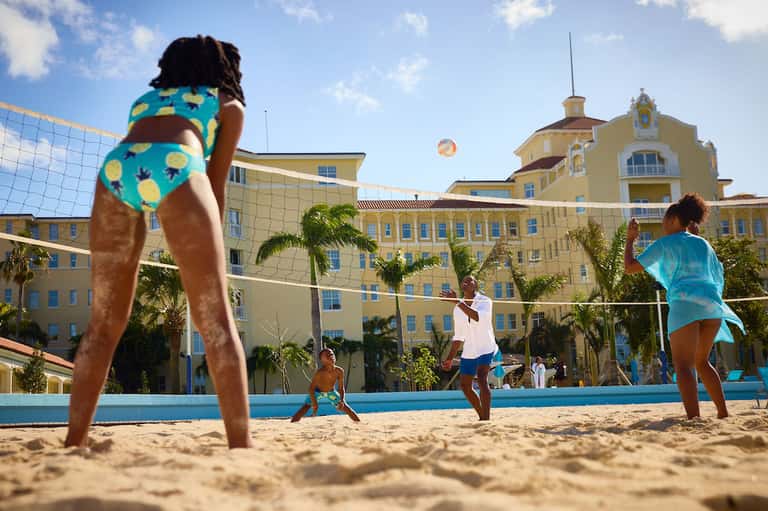 People playing beach volleyball in front of yellow resort building