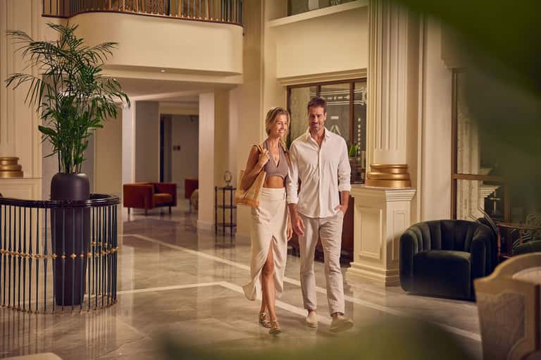 Couple walking through modern hotel lobby with high ceilings, marble floors, and contemporary furnishings