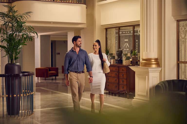 Modern hotel lobby with couple walking past decorative plants and elegant furnishings