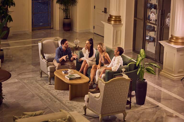 Elegant hotel lobby with guests conversing in seating areas surrounded by classical columns and marble flooring