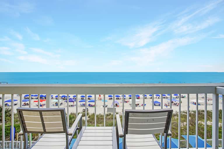 Beachfront view from deck with lounge chairs overlooking sandy beach and ocean