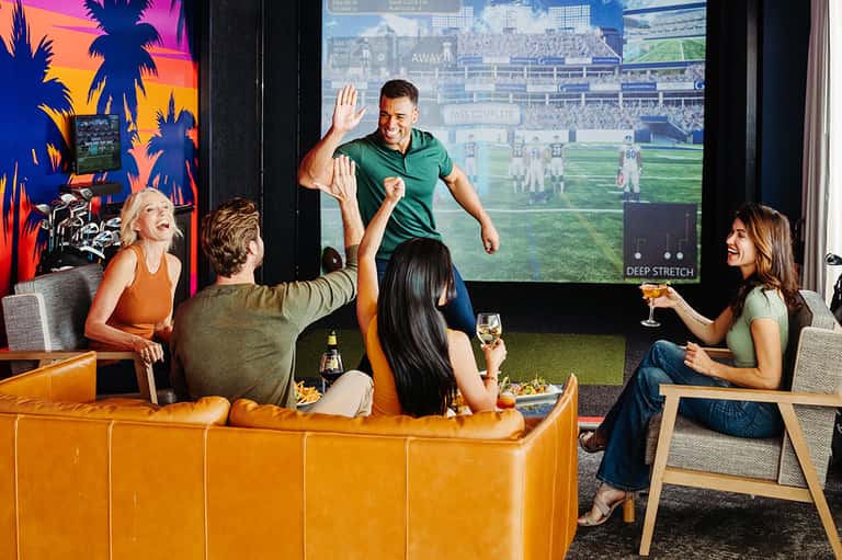 Group of people watching sports on large screen in modern lounge with orange furniture