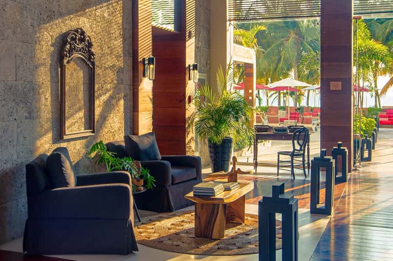 Hotel courtyard with arched stone entrance, black lounge chairs, palm plants, and water feature