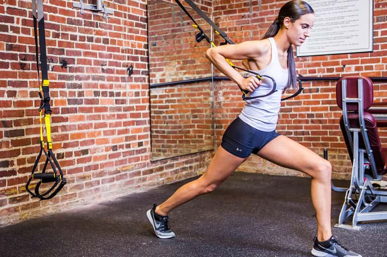 Fit woman performing suspension training exercise with TRX straps in brick-walled gym