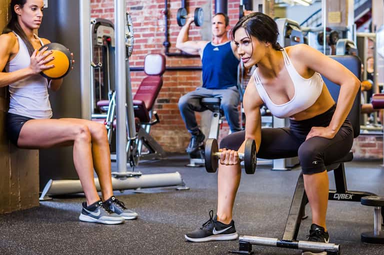 Women exercising with dumbbells and weights in a modern gym with brick walls