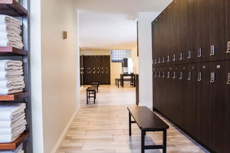 Spa locker room with dark wooden lockers, folded towels on shelves, and wooden benches in hallway