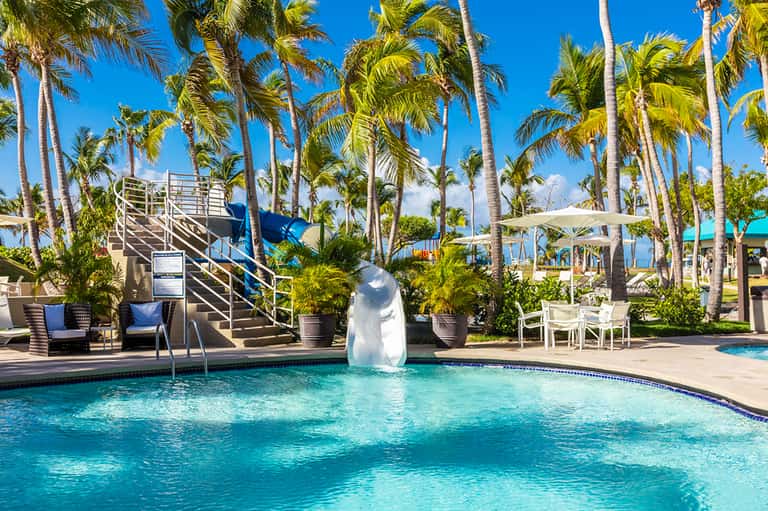 Resort pool with waterslide surrounded by palm trees and lounge chairs