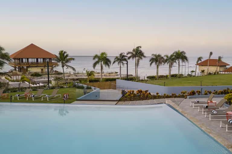 Beachfront resort with multiple blue pools, palm trees, ocean views, and tropical landscape at sunset