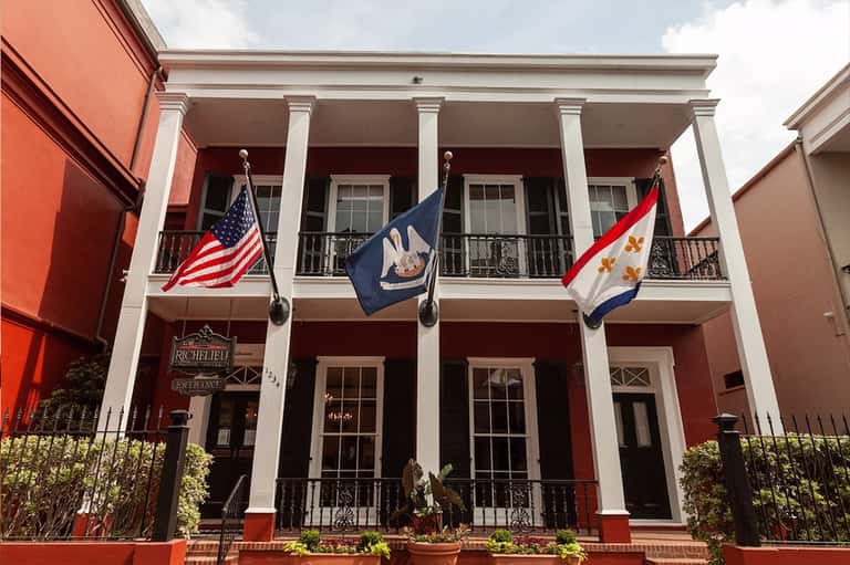 Historic red brick building with white columns and three flags: American, Louisiana state, and French colonial flags