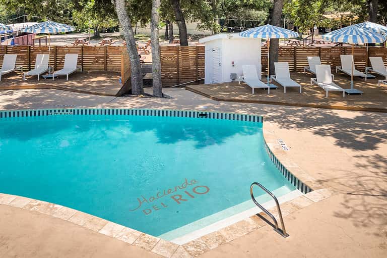 Resort pool with wooden fence and striped umbrellas surrounded by trees and shade