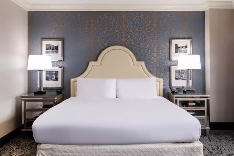 Elegant bedroom with cream upholstered headboard against blue damask wallpaper